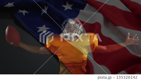 Celebrating football player raising football in studio, wearing helmet, jersey and pads on USA flag Celebrating football player raising football in studio, wearing helmet, jersey and pads on USA flag 135320142