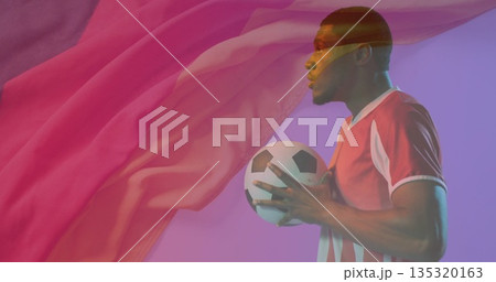 Soccer player wearing red jersey holding soccer ball in studio, with floating fabric, copy space Soccer player wearing red jersey holding soccer ball in studio, with floating fabric, copy space 135320163