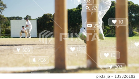 Jumping bowler delivering ball on park cricket field, with stumps and social icons 135320182