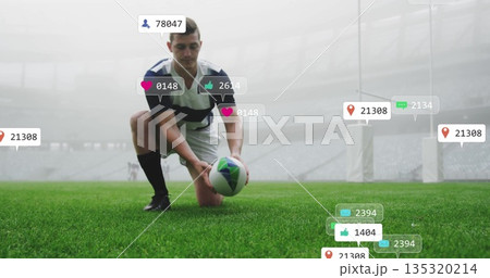 Kneeling rugby player in striped jersey placing rugby ball on pitch at stadium, with floating icons 135320214