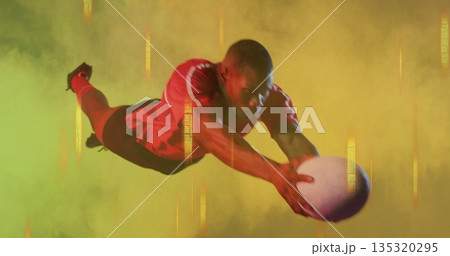 Diving athlete catching white ball in studio, wearing red jersey, black shorts, cleats, colored fog 135320295
