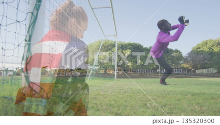 Catching teenage goalkeeper in jersey grabbing soccer ball on pitch with net, gloves, second ball Catching teenage goalkeeper in jersey grabbing soccer ball on pitch with net, gloves, second ball 135320300