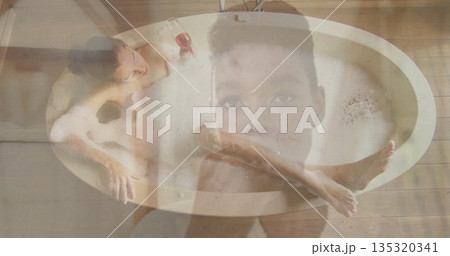 Reclining woman soaking in oval bathtub on plank floor, with foam, red wine glass, double exposure Reclining woman soaking in oval bathtub on plank floor, with foam, red wine glass, double exposure 135320341