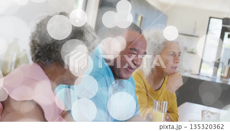 Three retirees chatting over orange juice in clear glasses at dining table in home kitchen Three retirees chatting over orange juice in clear glasses at dining table in home kitchen 135320362