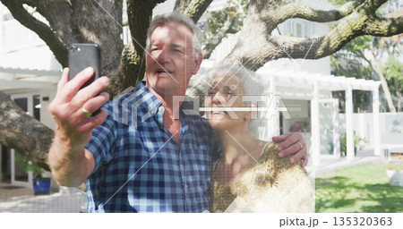 Taking selfie, sweater-clad woman and plaid-shirt man under oak tree in backyard, with smartphone Taking selfie, sweater-clad woman and plaid-shirt man under oak tree in backyard, with smartphone 135320363