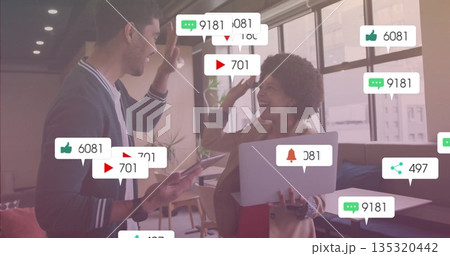 High-fiving colleagues in office lounge with tablet smartphone notification icon overlays 135320442