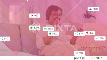 Waving mature woman using tablet, sitting on sofa in living room, displaying social metrics Waving mature woman using tablet, sitting on sofa in living room, displaying social metrics 135320446