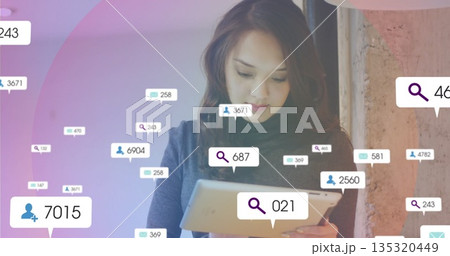 Asian woman holding tablet and checking floating notification icons in office, with concrete wall 135320449
