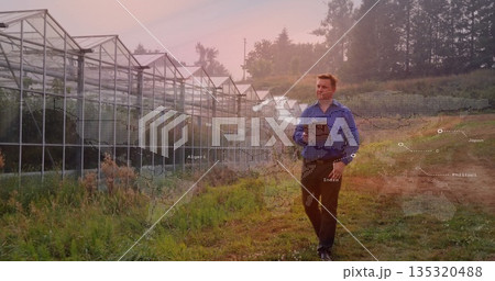 Walking researcher in shirt using tablet in field near greenhouse, world map overlay, copy space Walking researcher in shirt using tablet in field near greenhouse, world map overlay, copy space 135320488