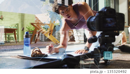 Holding instructor plank, talking into DSLR camera in home gym by glass door, in leggings 135320492