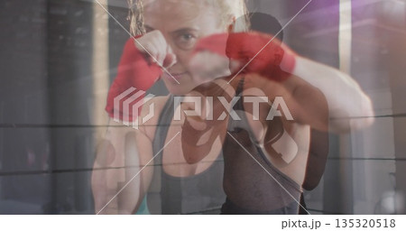 Guarding boxer in tank top raising fists in boxing ring, with red wraps and black gloves 135320518