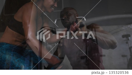 Female trainer leaning close to guide male client doing cable pushdown in gym, with rope attachment Female trainer leaning close to guide male client doing cable pushdown in gym, with rope attachment 135320536