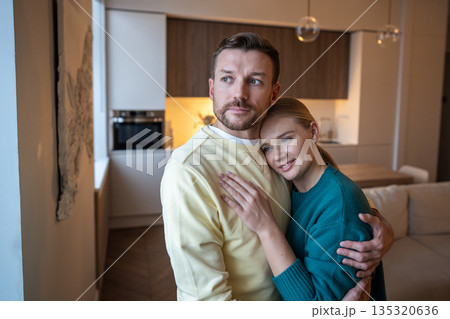 Positive pensive couple man and woman embracing and looking at window with pensive expression. 135320636
