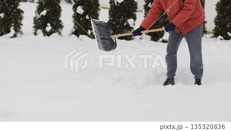 Young man cleans snow with a shovel after snowfall background of the house in winter. 135320836