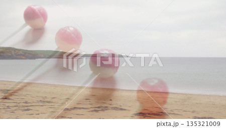 Four translucent round pink-and-white lollipops with sticks drifting above sandy beach, cloudy sky 135321009