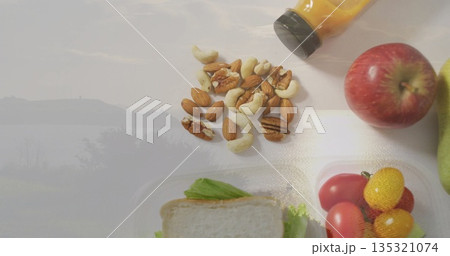 Arranging nut mix on white countertop with sandwich box, cherry tomatoes, juice bottle, apple, pear Arranging nut mix on white countertop with sandwich box, cherry tomatoes, juice bottle, apple, pear 135321074