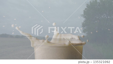 Erupting paper cup containing creamy beige liquid at lakeside under cloudy sky, droplets midair 135321092