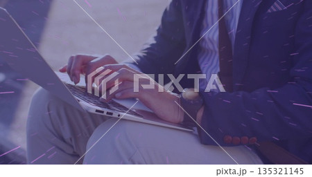 Mature Asian man wearing business attire typing on laptop in outdoor courtyard, with wristwatch 135321145