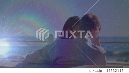 Hugging couple leaning toward ocean on boardwalk, with wooden bench and railing beneath sunflare Hugging couple leaning toward ocean on boardwalk, with wooden bench and railing beneath sunflare 135321154