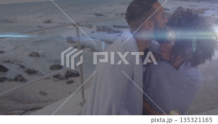Hugging couple kissing on coastal promenade, with light gray blanket, lens flare, copy space 135321165