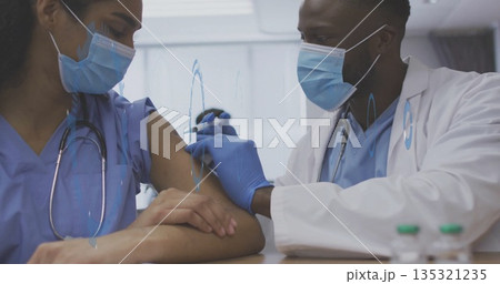 Injecting doctor administering vaccine into nurse in scrubs' arm at clinic, with syringe and vials Injecting doctor administering vaccine into nurse in scrubs' arm at clinic, with syringe and vials 135321235