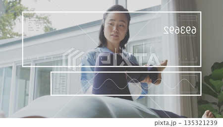 Stretching Korean therapist holding patient leg on table in therapy room with digital overlays 135321239