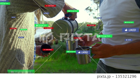 Sweater-clad woman pouring from carafe into friend's mug on lake shore, with floating notifications 135321296