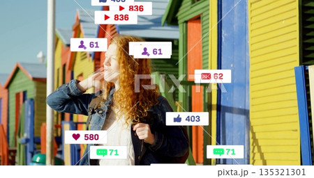 Standing redhead wearing denim jacket and backpack on boardwalk, with floating social media icons 135321301