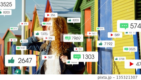 Calling redhead woman wearing denim jacket on smartphone at beach huts with floating notifications 135321307
