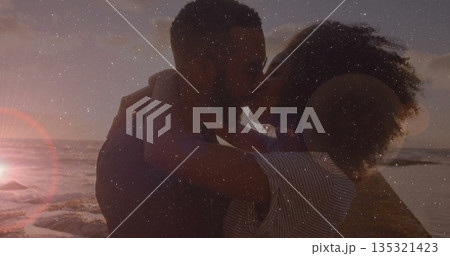 Kissing couple wearing striped top embracing on wooden pier over ocean at sunset, with lens flare 135321423