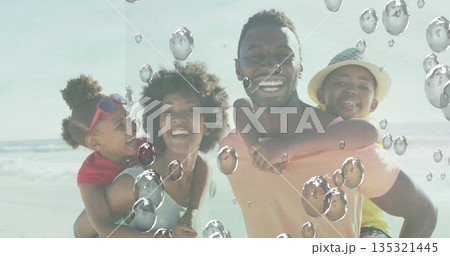 Smiling family carrying children on backs at sandy seashore, with straw sun hat and red sunglasses Smiling family carrying children on backs at sandy seashore, with straw sun hat and red sunglasses 135321445