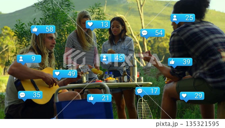 Group of friends playing guitar and sharing snacks in grassy meadow, with collapsible picnic table Group of friends playing guitar and sharing snacks in grassy meadow, with collapsible picnic table 135321595