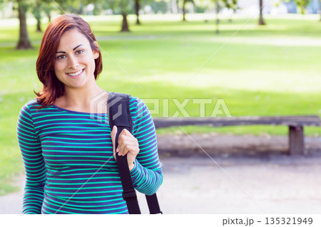 Female student wearing striped shirt holding black shoulder bag near park bench, copy space Female student wearing striped shirt holding black shoulder bag near park bench, copy space 135321949