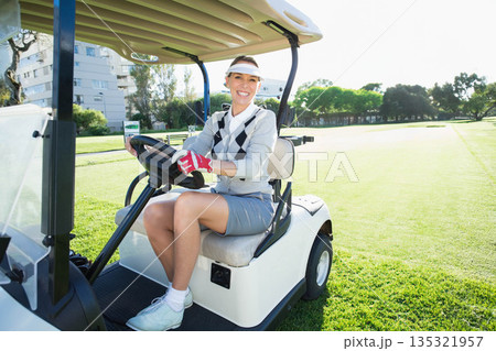 Senior woman sitting in golf cart on fairway gripping steering wheel wearing visor and golf glove 135321957
