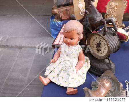 Vintage items and toys at flea market in Europe, Italy. Doll in dress and table clock. Old items and art. Vintage items and toys at flea market in Europe, Italy. Doll in dress and table clock. Old items and art. 135321975
