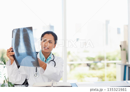 Indian woman doctor examining chest X-ray film in white lab coat at clinic desk with stethoscope 135321981