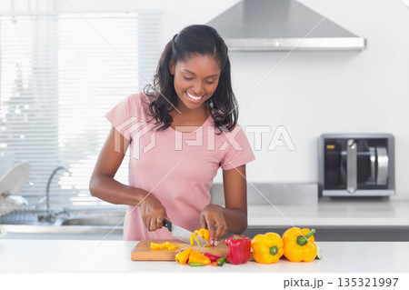 African American woman chopping yellow peppers with knife on board at white kitchen countertop 135321997