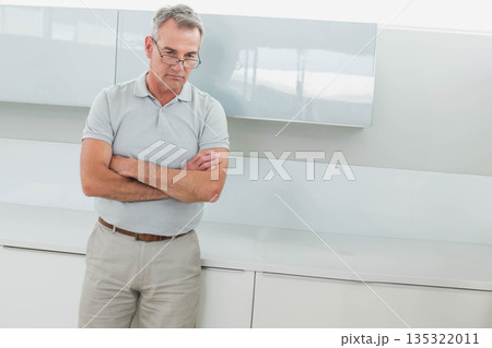 Man standing, pondering in modern kitchen wearing reading glasses near grey countertop, copy space 135322011