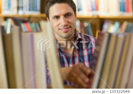 Man standing between bookshelves in library, looking through gap and selecting volume 135322049