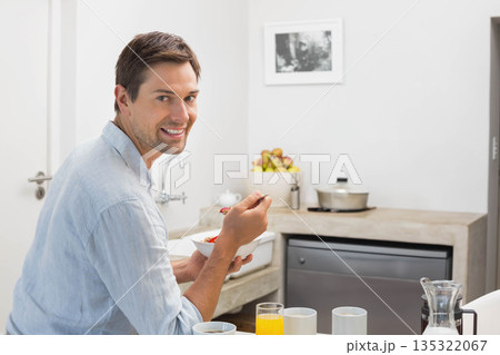 Man smiling while holding white cereal bowl and spoon at kitchen counter, copy space 135322067