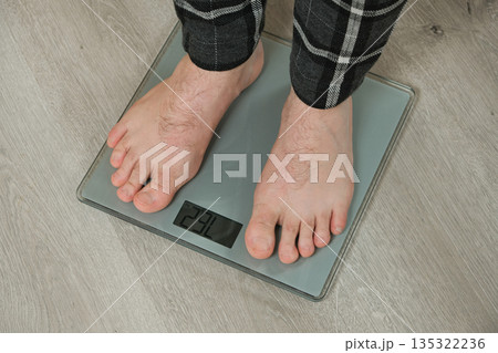 Man weighing himself on modern weighing scales at home, close-up of bare feet. Man weighing himself on modern weighing scales at home, close-up of bare feet. 135322236
