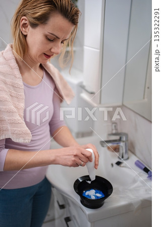 Woman preparing hair dye in bathroom following instructions 135322291