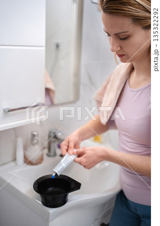 Young woman preparing hair dye in a bowl in bathroom 135322292