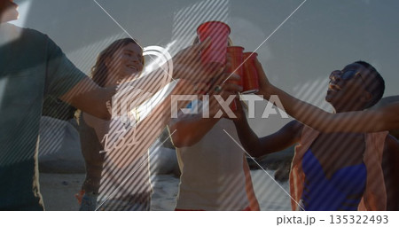 Toasting group of five adults in swimwear raising red plastic cups on sandy beach, sunset glow 135322493
