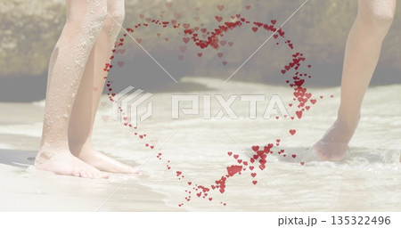 Children's legs and feet wading in shallow beach water, with wet sand clinging and heart overlay 135322496