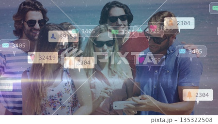 Leaning in six friends wearing sunglasses viewing smartphone on beach, with social media icons 135322508