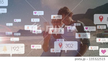Posing mother-son duo taking selfie on beach at sunset, with smartphone floating notification icons Posing mother-son duo taking selfie on beach at sunset, with smartphone floating notification icons 135322515