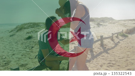 Kneeling man presenting ring box to woman adjusting sunhat on beach path, with fence and dunes Kneeling man presenting ring box to woman adjusting sunhat on beach path, with fence and dunes 135322543