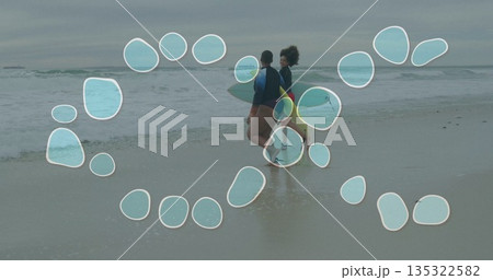 Walking women surfers carrying surfboards at wet sandy shoreline, with rash guards and board shorts 135322582
