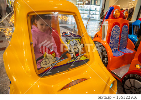 Little girl riding coin operated toy car attraction in shopping mall kids area. Childhood entertainment moment, family leisure activity and everyday fun experience in real life commercial environment 135322916
